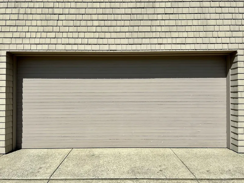 Closed tan sectional garage door awaiting broken spring repair